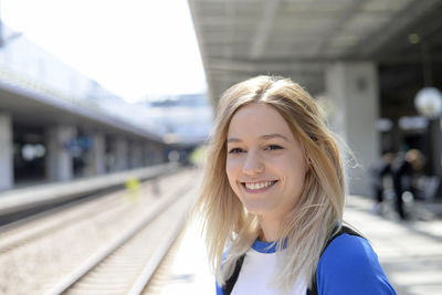 Smiling young woman standing at railroad station