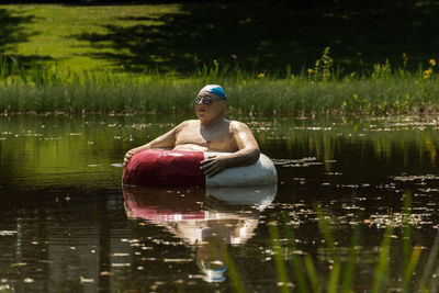 Shirtless man with inflatable ring swimming in lake 