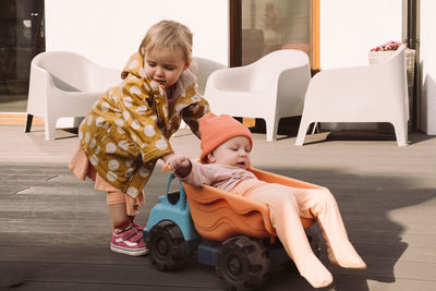 Brother sister giving a ride to baby sister in big toy car outdoors. children having fun near house