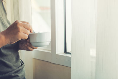 Midsection of man holding coffee cup at home