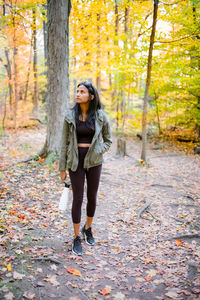 Full length portrait of woman standing by tree in forest