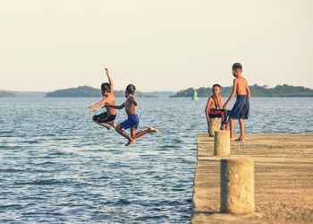 Friends looking at boys diving into sea against clear sky