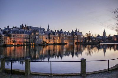 Buildings by river in city during sunset