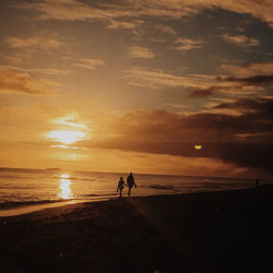 Silhouette people walking on beach against sky during sunset