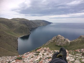 Low section of man on rock by lake against sky