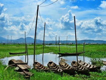 Old wooden bots on grassy field by river against cloudy sky