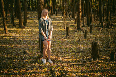 Full length portrait of woman standing on tree trunk in forest