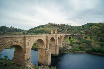 Arch bridge over river against cloudy sky