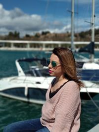 Woman wearing sunglasses while sitting at lake against sky