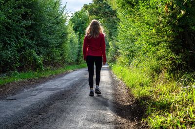 Rear view of woman walking on road amidst plants