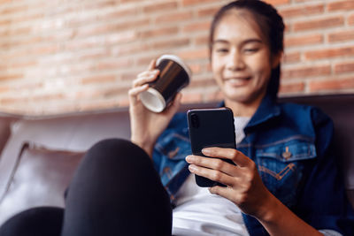 Woman drinking coffee cup while using smart phone at home