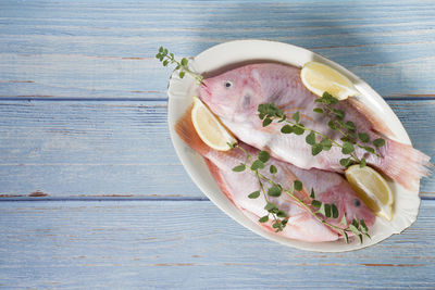 Raw fresh pink tilapia fish lies on a platter surrounded by yellow lemons