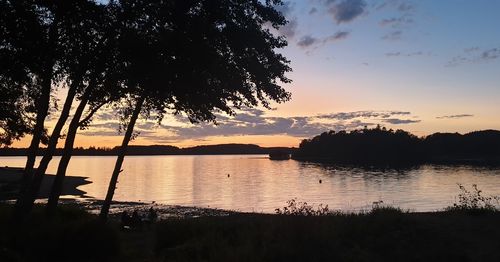 Silhouette trees by lake against sky during sunset