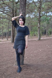 Full length portrait of smiling young woman standing in forest