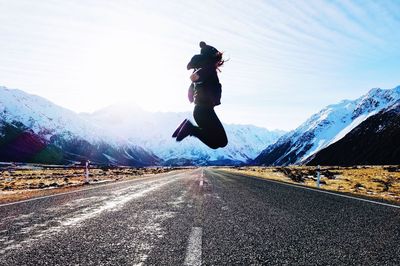 Woman jumping on road against mountain during winter