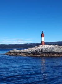 Lighthouse by sea against clear blue sky
