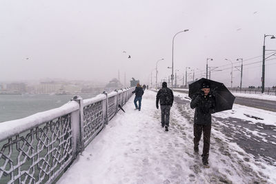 People walking on snow covered city against sky