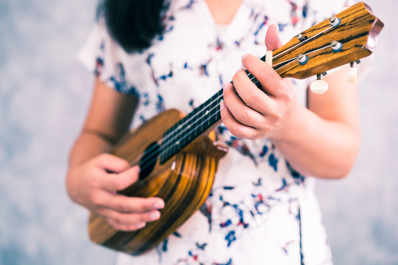 MIDSECTION OF WOMAN PLAYING GUITAR AT MUSIC