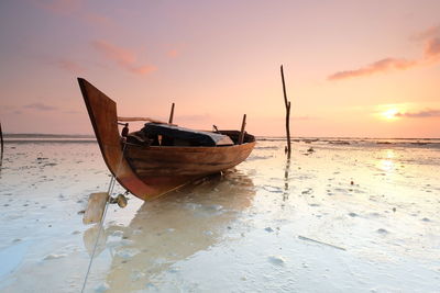 Boat moored on beach against sky during sunset