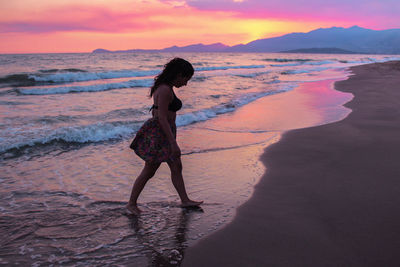 Woman standing on beach against sky during sunset