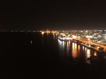 Illuminated city by river against clear sky at night