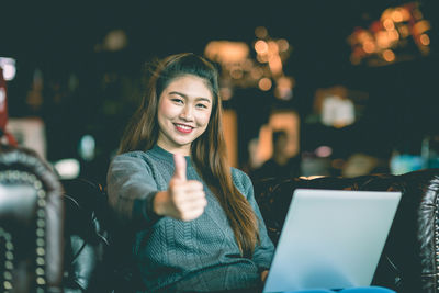 Portrait of smiling young woman using mobile phone at night