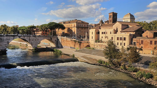 Arch bridge over river by buildings against sky