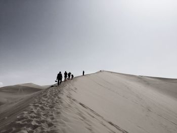 Rear view of people walking on sand dune at desert against clear sky