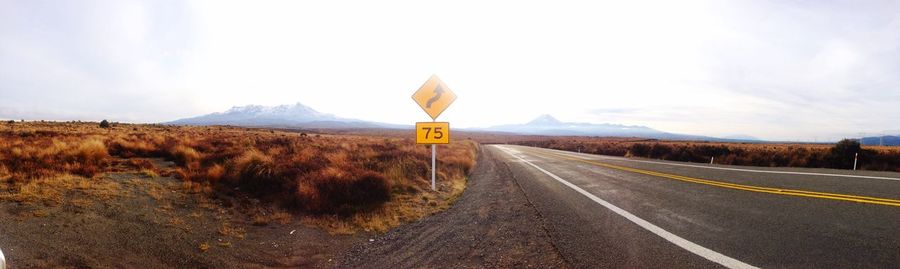 Panoramic view of road by field against sky