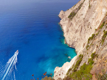 High angle view of rocky cliff by blue sea