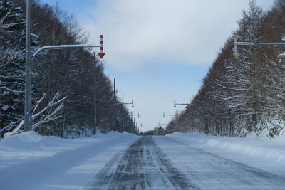 Arrow signs on pole over snow covered road against sky