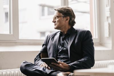 Mature businessman holding tablet looking out of window