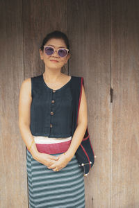 Portrait of woman wearing sunglasses standing against wall