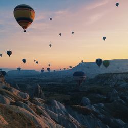 Hot air balloons flying over rocks against sky during sunset