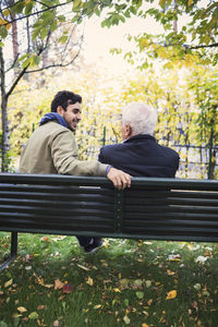 Rear view of caretaker looking at senior man while sitting on bench at park