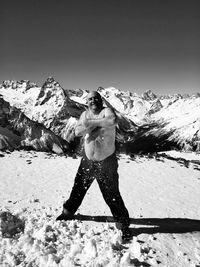 Portrait of shirtless man rubbing snow on self while standing against snowcapped mountains