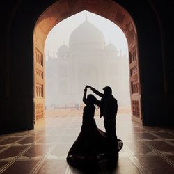 Silhouette man photographing woman in building