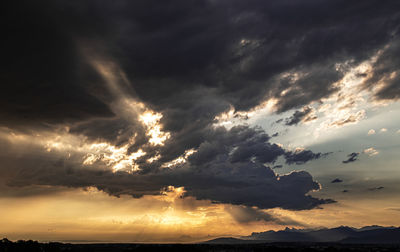 Low angle view of sunlight streaming through clouds during sunset