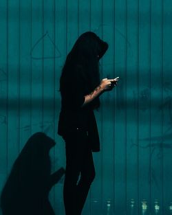 Woman using smart phone against blue wall