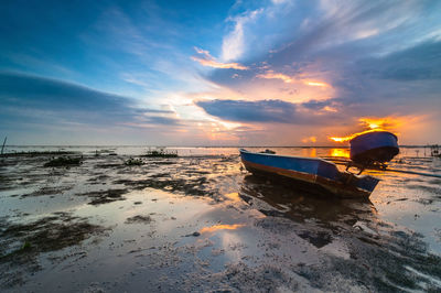 Boat moored on beach against sky during sunset