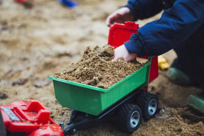 Cropped image of kid playing with toy truck on sand at beach