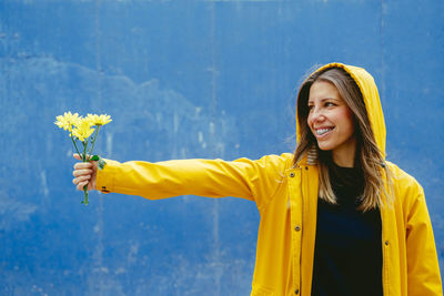 Happy woman holding yellow daisy against blue background