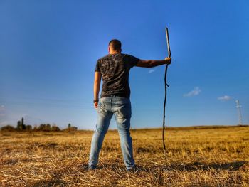 Rear view of man holding stick while standing on grass against sky