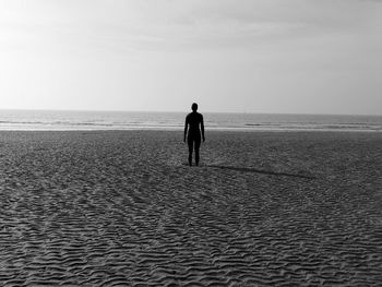 Rear view of man standing on beach against sky