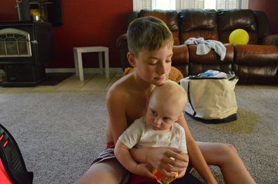 Shirtless boy with brother sitting on carpet at home