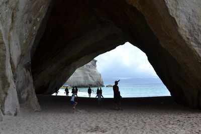 People below rock formation at beach