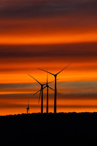 Silhouette wind turbines on field against sky during sunset