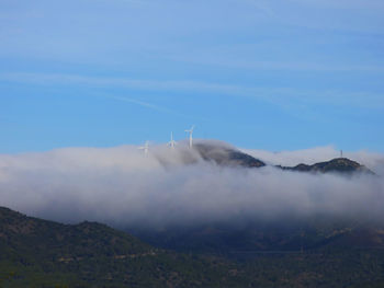 Windmills on field during foggy weather against sky