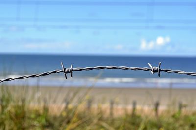 Barbed wire fence on field against sky