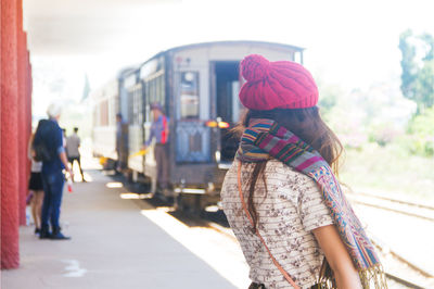 Woman wearing knit hat and scarf while standing at railroad station platform